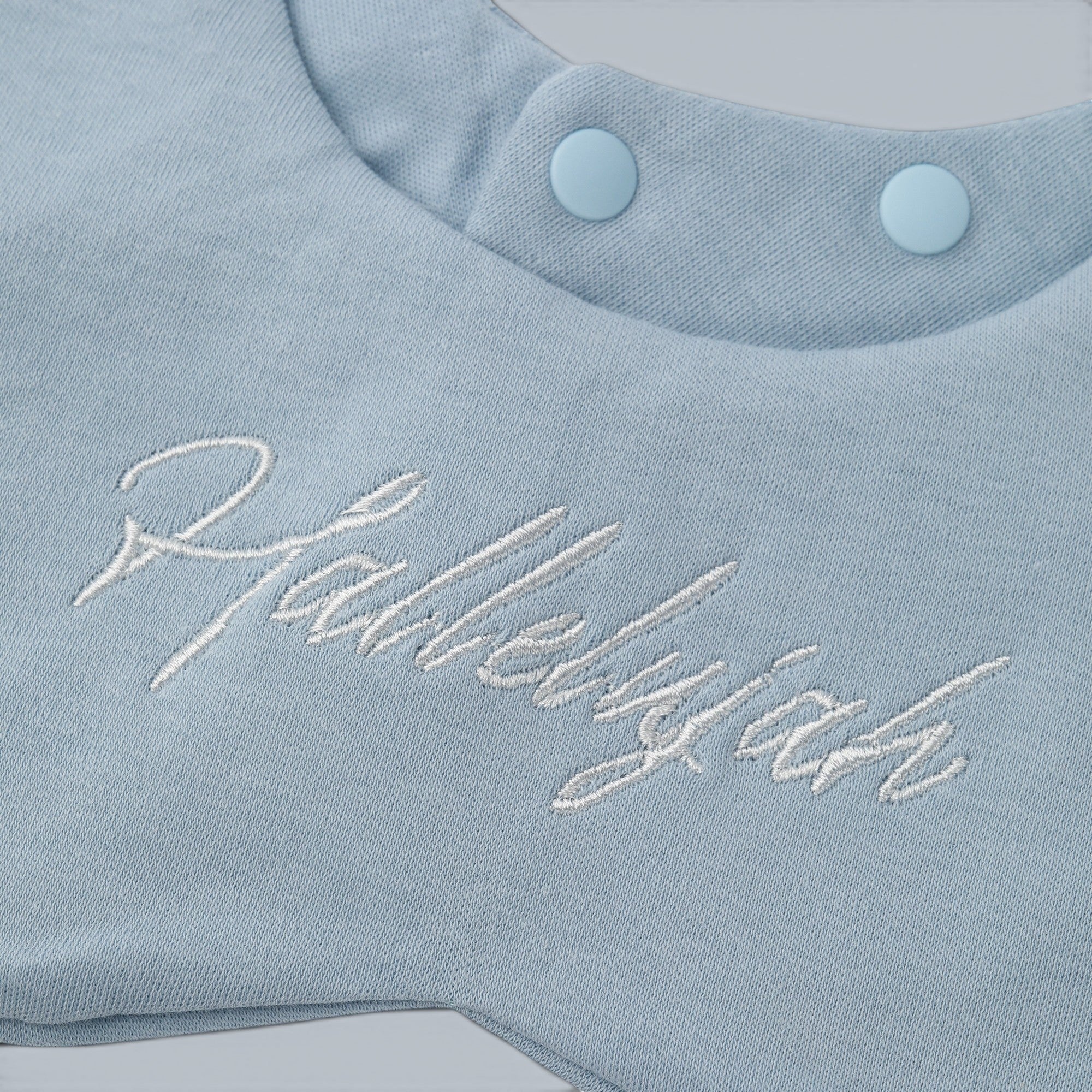 Shalom Living baby blue cotton bib with white "Hallelujah" embroidery and snap closure.