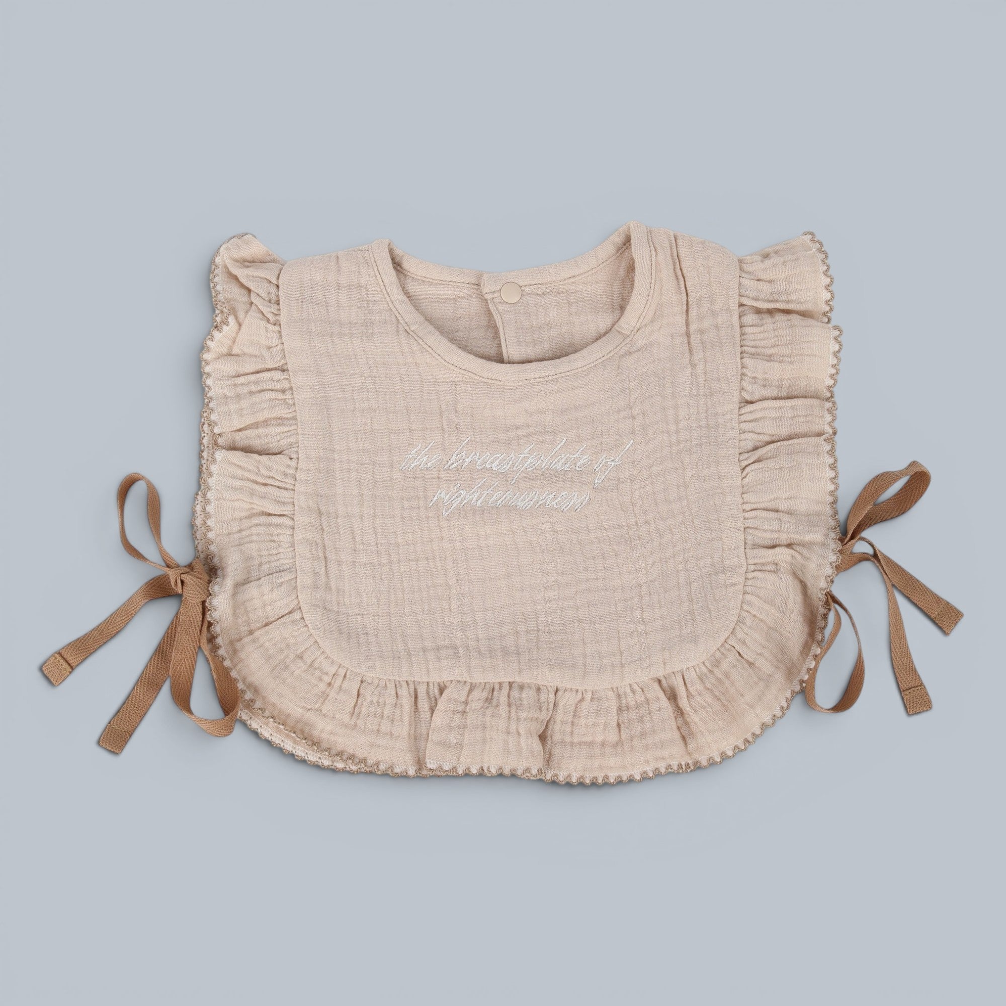 Shalom Living beige cotton ruffle bib with embroidered text and tie closures.