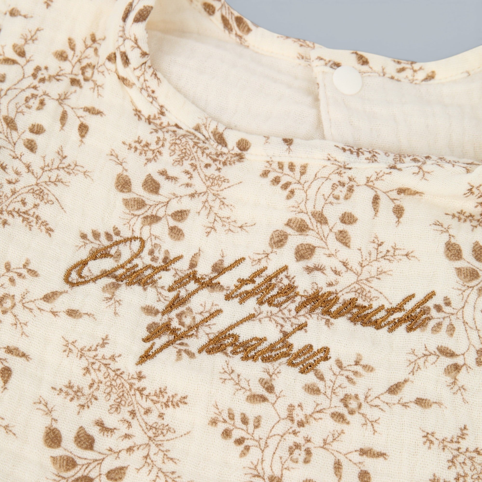 Shalom Living cream cotton ruffle bib with brown floral print and embroidered text "Out of the mouth of babes."
