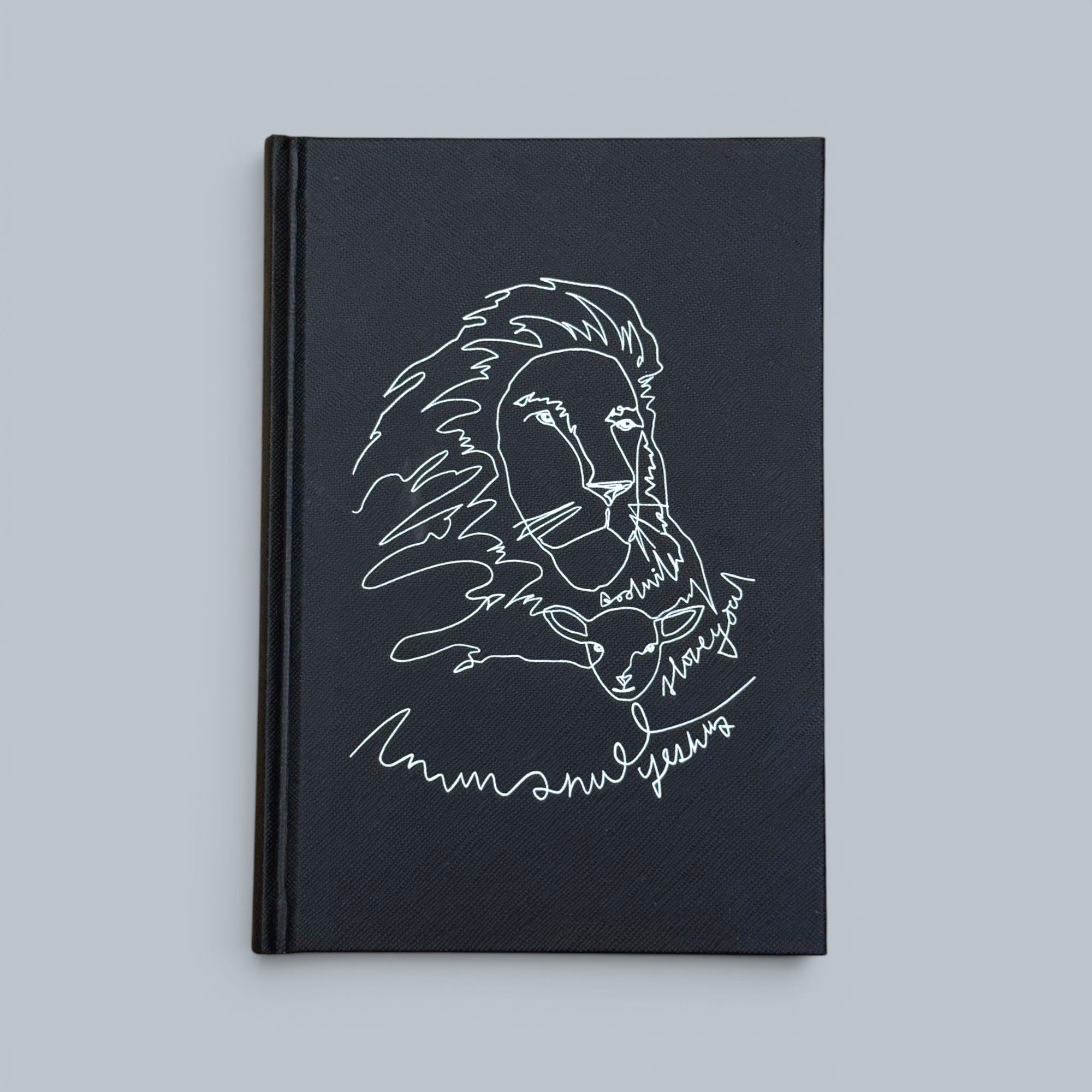 Shalom Living black hardcover journal featuring a white line drawing of a lion and a lamb, with text "Emmanuel Jesus".