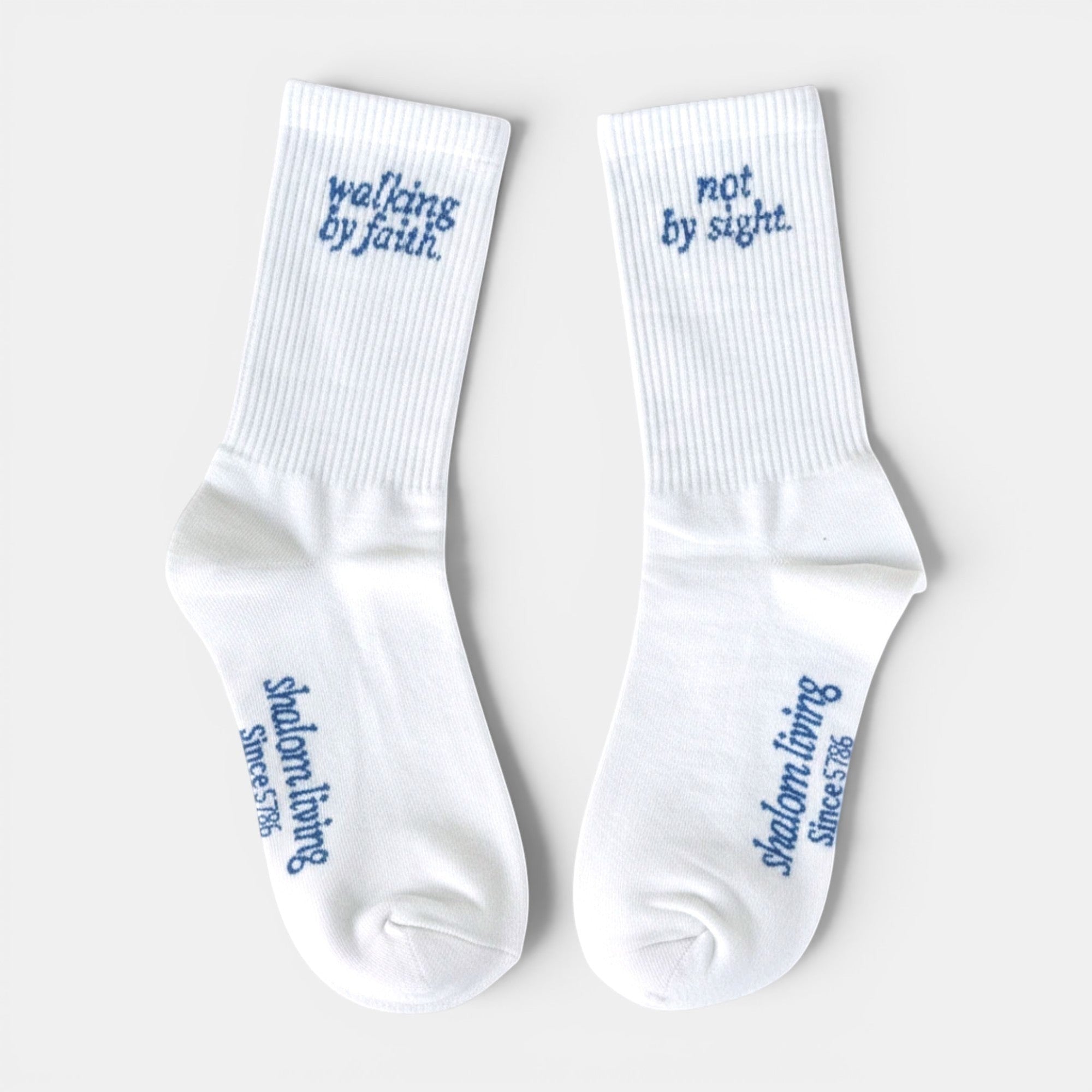 Shalom Living white cotton crew socks with blue text reading "walking by faith" on one and "not by sight" on the other.
