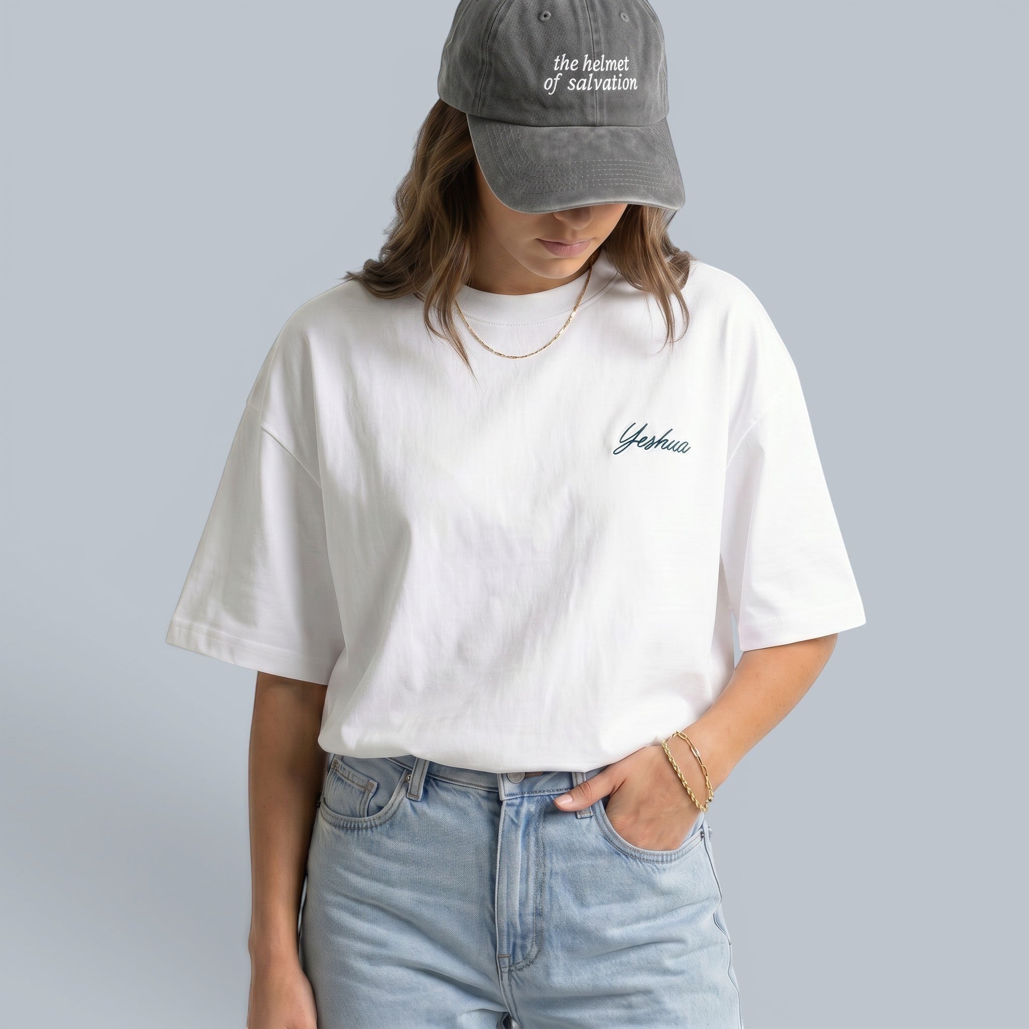Shalom Living white cotton boxy t-shirt with subtle blue Yeshua embroidery on the chest, worn by a woman with light wash denim.