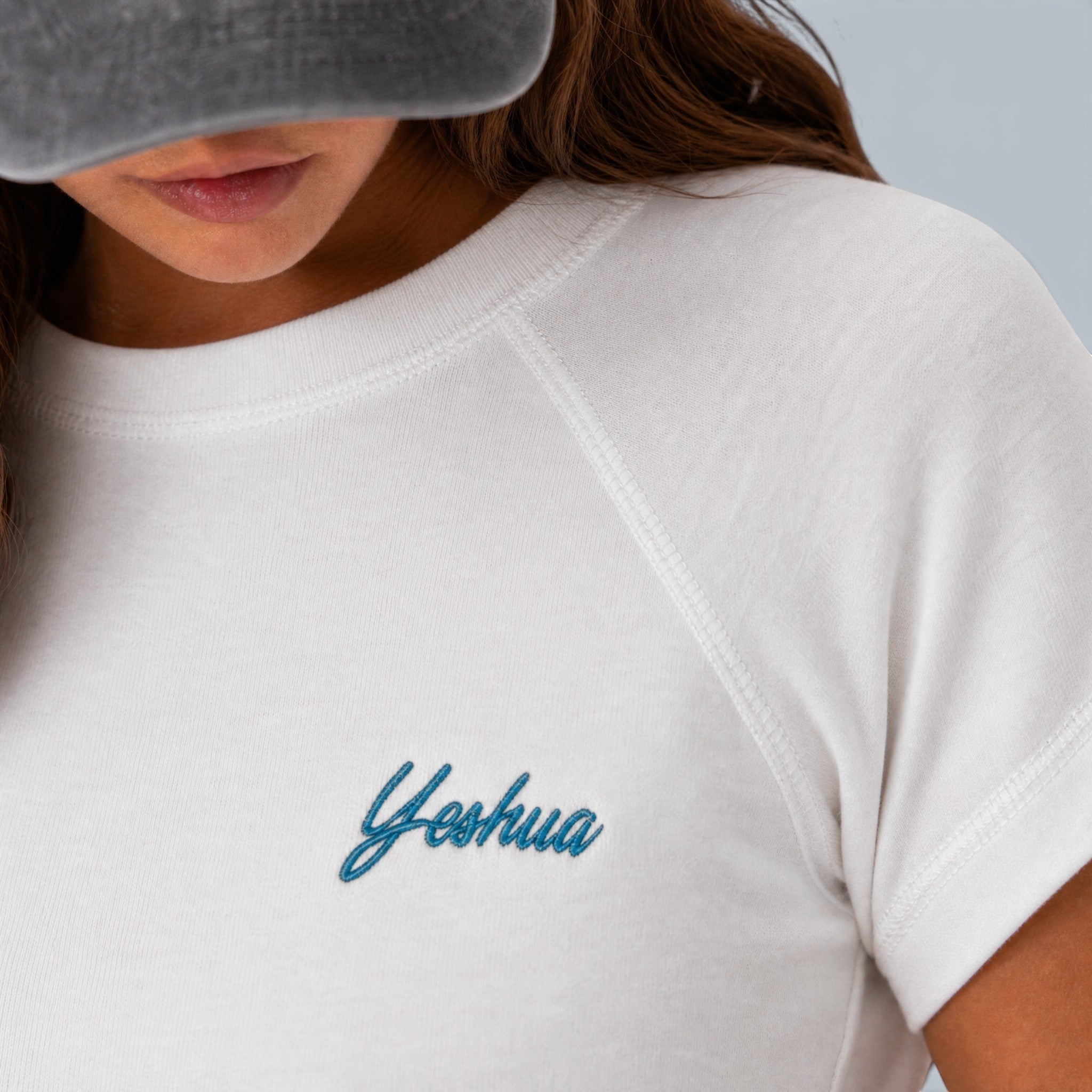 Shalom Living white fitted t-shirt with blue embroidered "Yeshua" text on the chest, made of soft stretchy cotton.