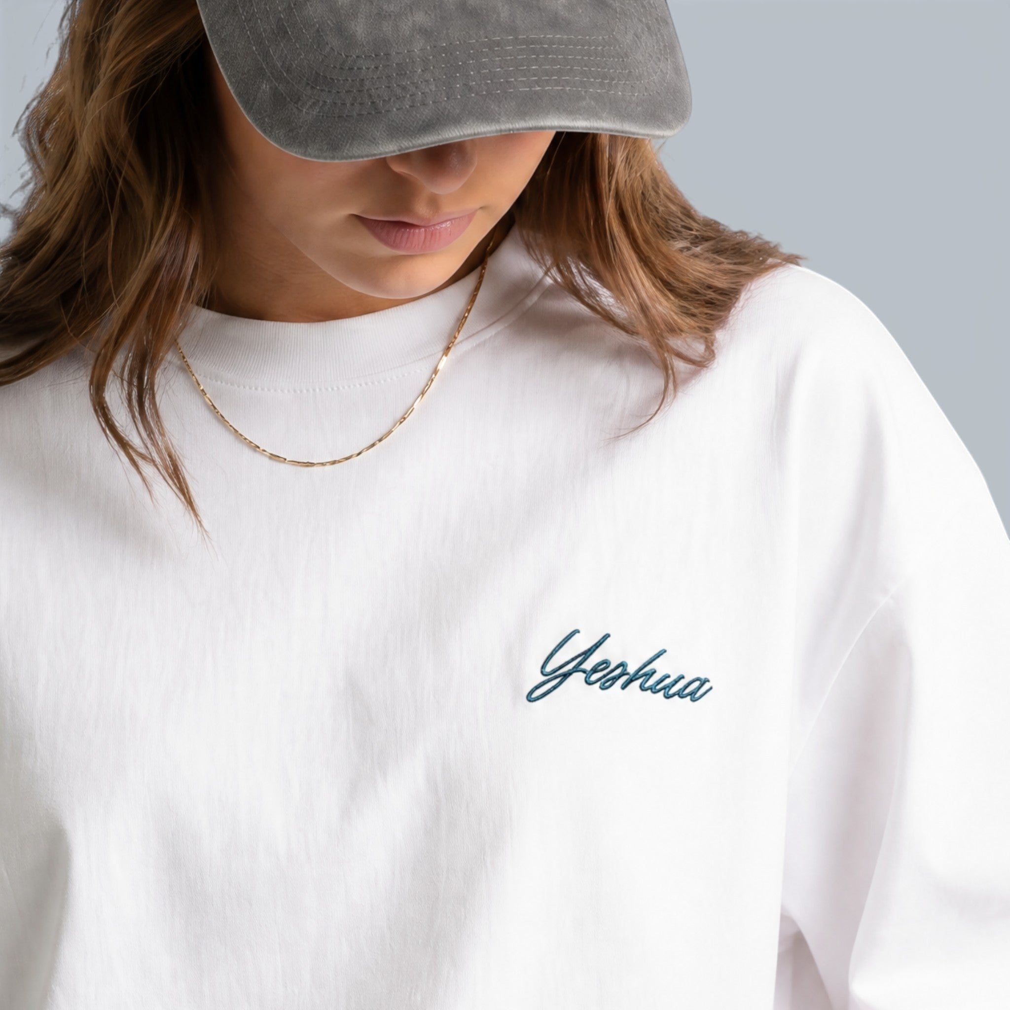 Shalom Living white cotton boxy t-shirt with subtle teal Yeshua embroidery on the chest, worn by a woman.
