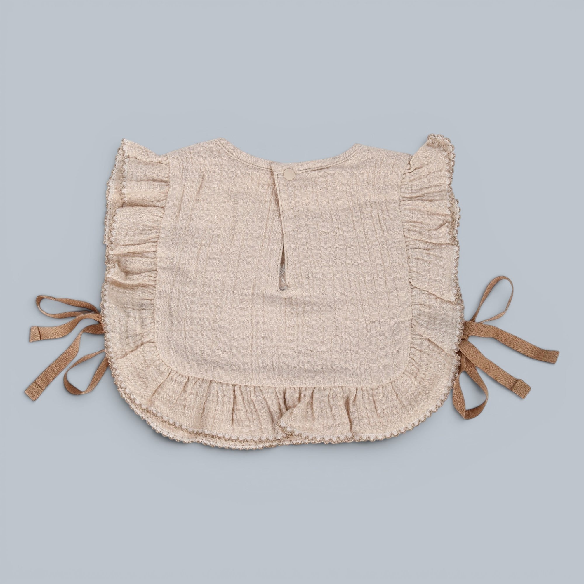 Shalom Living beige cotton gauze ruffle bib with embroidered scripture detail and tie closure.