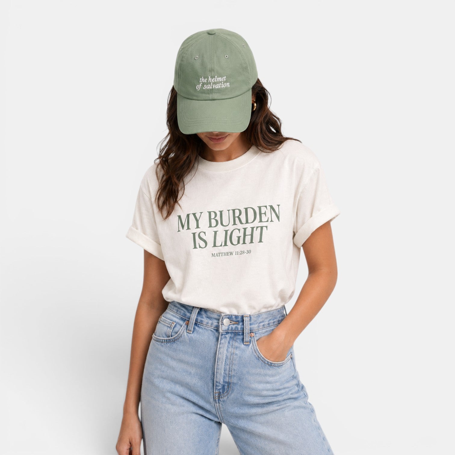 Shalom Living cream relaxed fit t-shirt with green text "MY BURDEN IS LIGHT MATTHEW 11:28-30". Model wears light wash jeans.