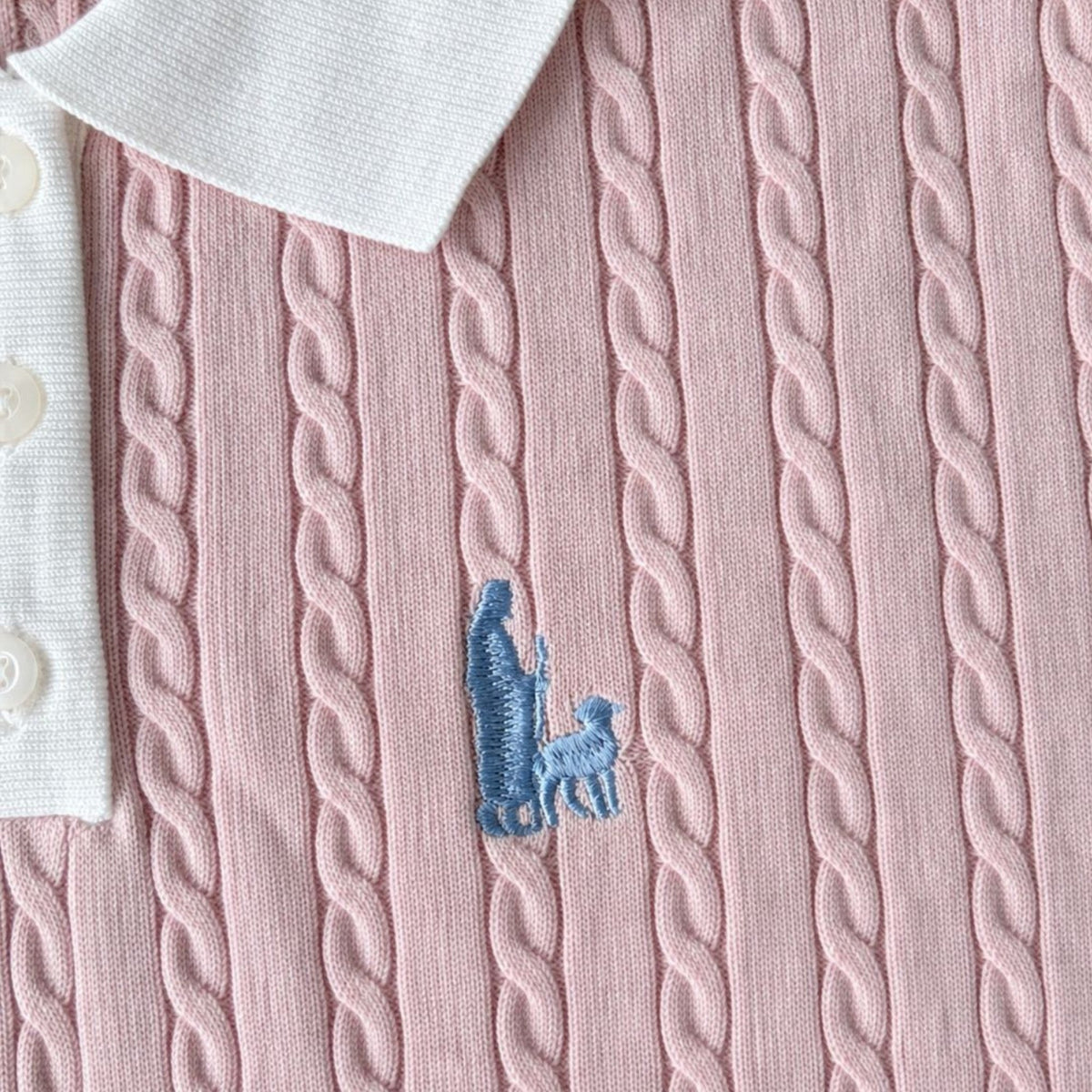 Shalom Living pink cable knit polo shirt with a white collar and blue embroidered shepherd and sheep detail.