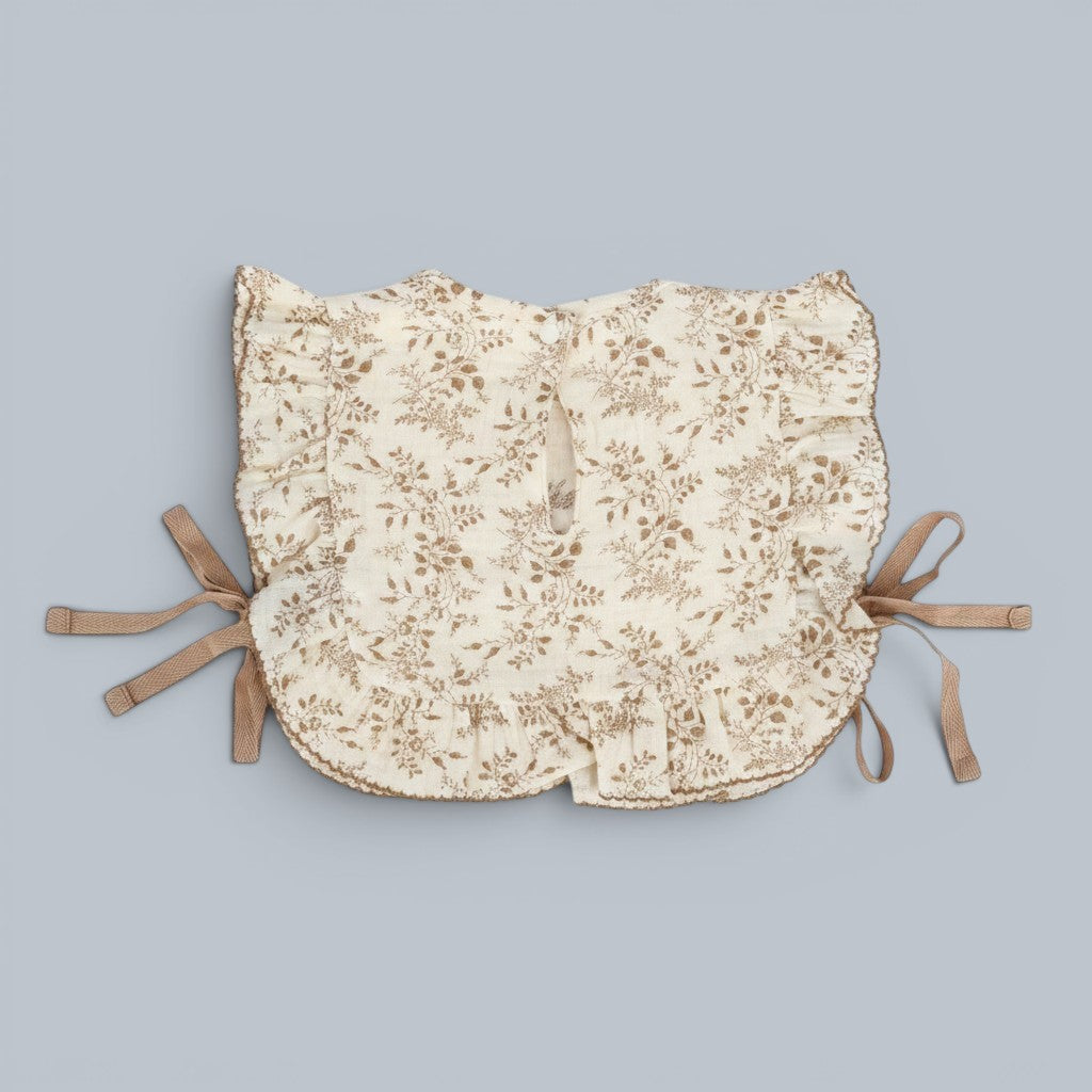 Shalom Living cream cotton ruffle bib with brown floral print and tie closures. Features embroidered scripture.