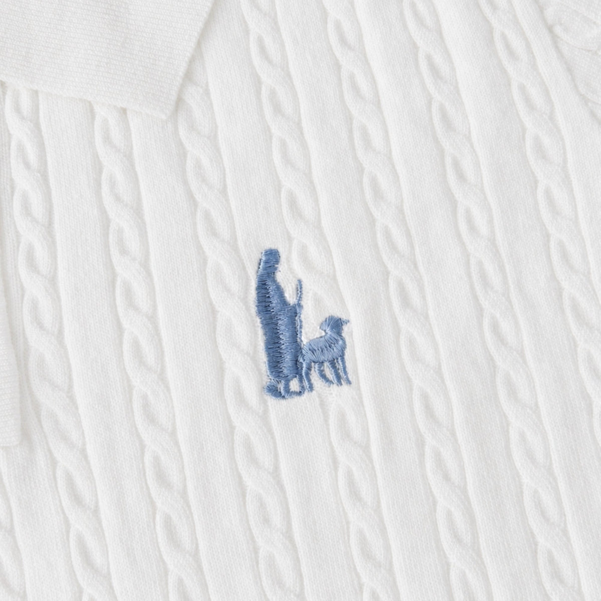 Shalom Living white cable knit polo shirt featuring a blue embroidered shepherd and sheep detail on the chest.