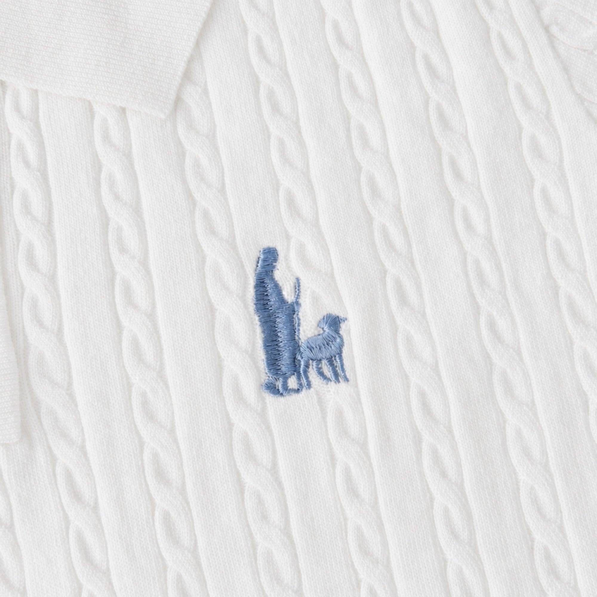 Shalom Living white cable knit polo shirt featuring a blue embroidered shepherd and sheep detail on the chest.