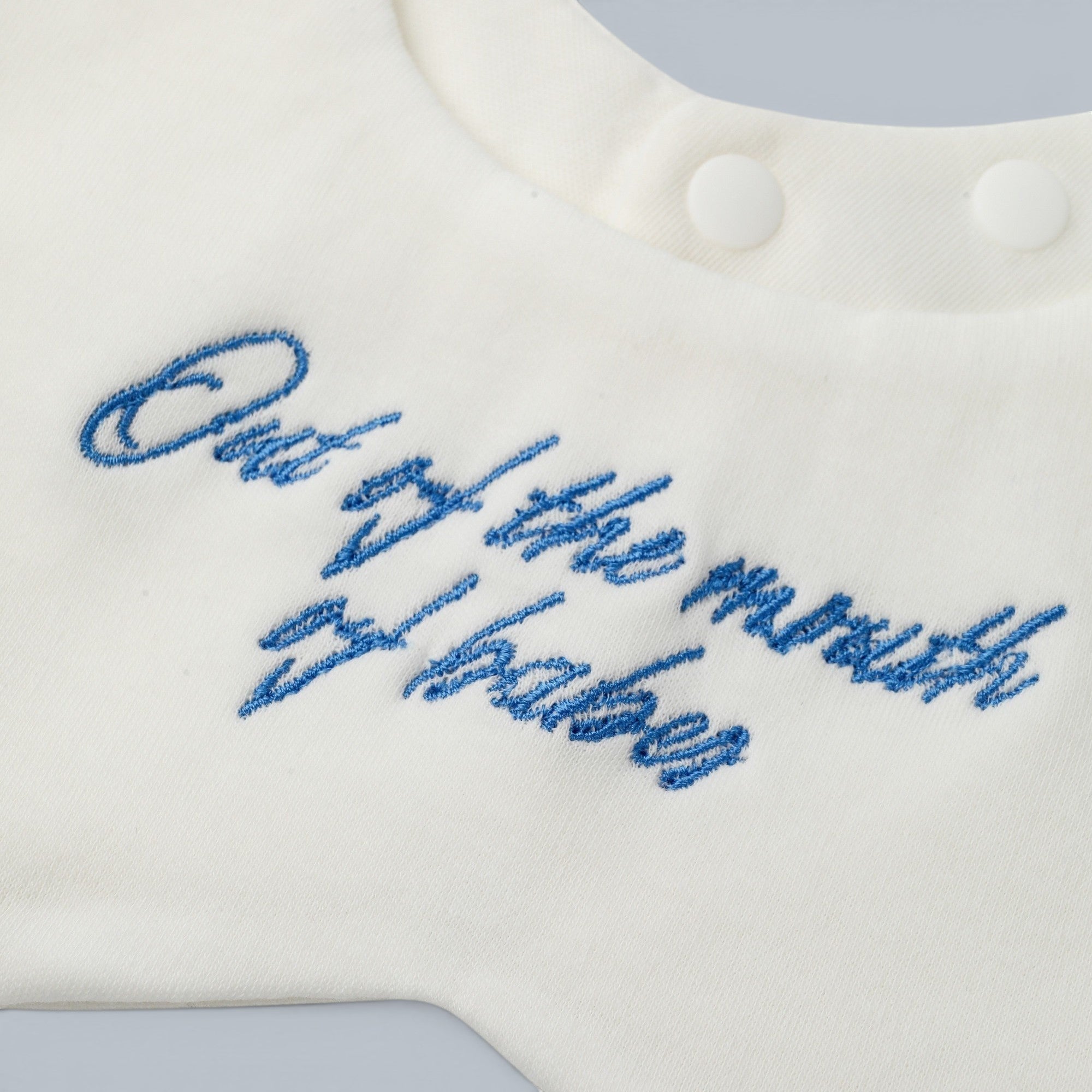 Shalom Living white cotton petal bib with blue embroidered text "Out of the mouth of babes".
